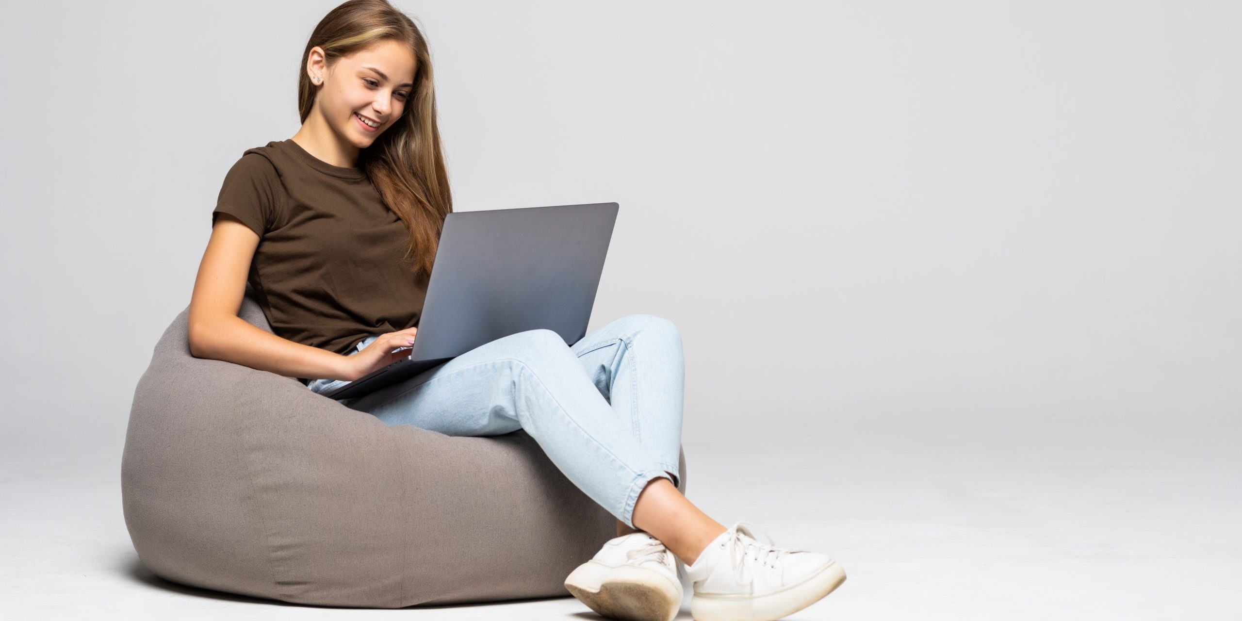 Happy young woman sitting on the floor using laptop on gray background